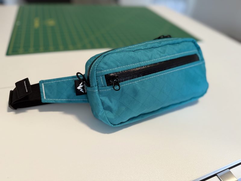 A small teal zippered bag resting on a white table with a cutting mat visible behind it.